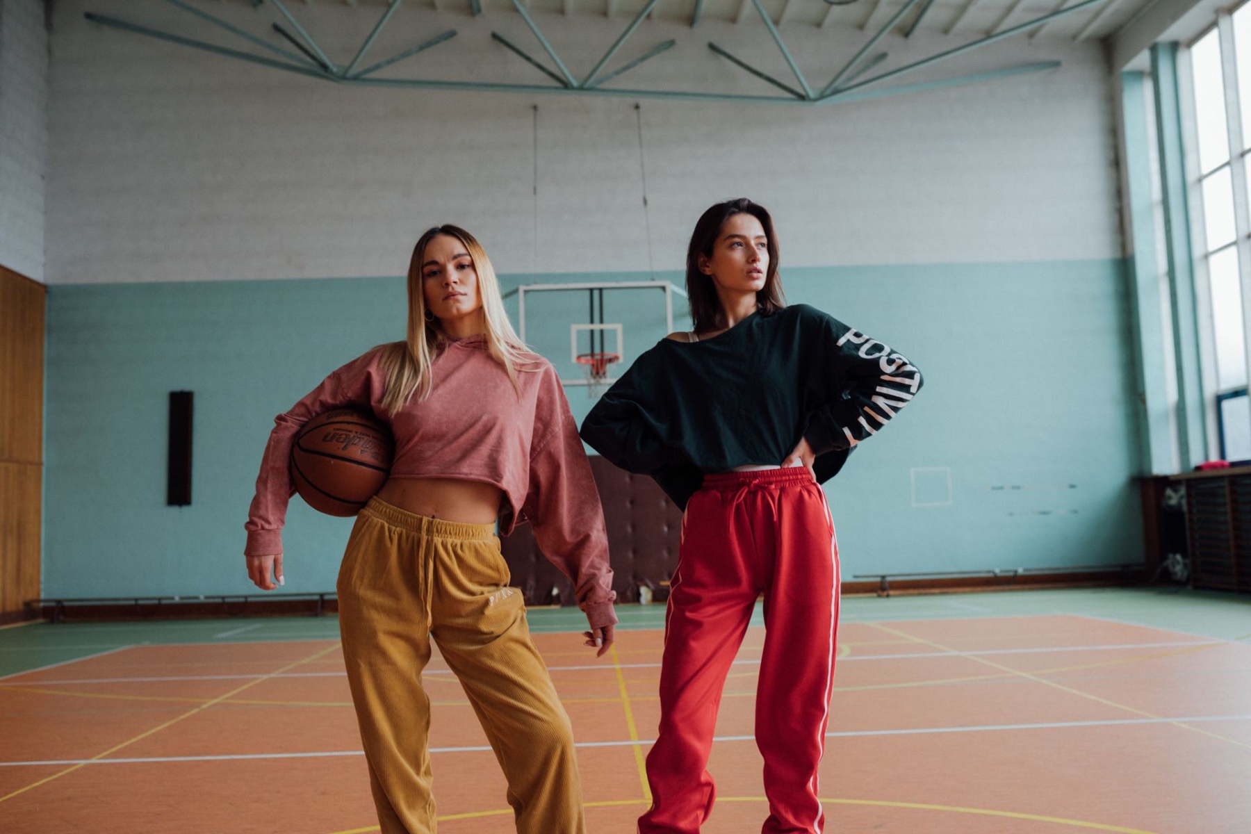 Two people wearing casual sports apparel on an indoor basketball court
